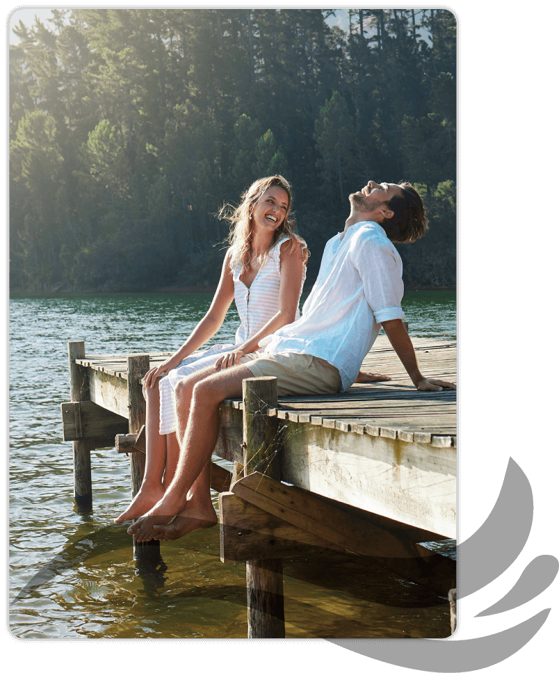 Couple sitting on dock laughing with feet hanging over the edge.