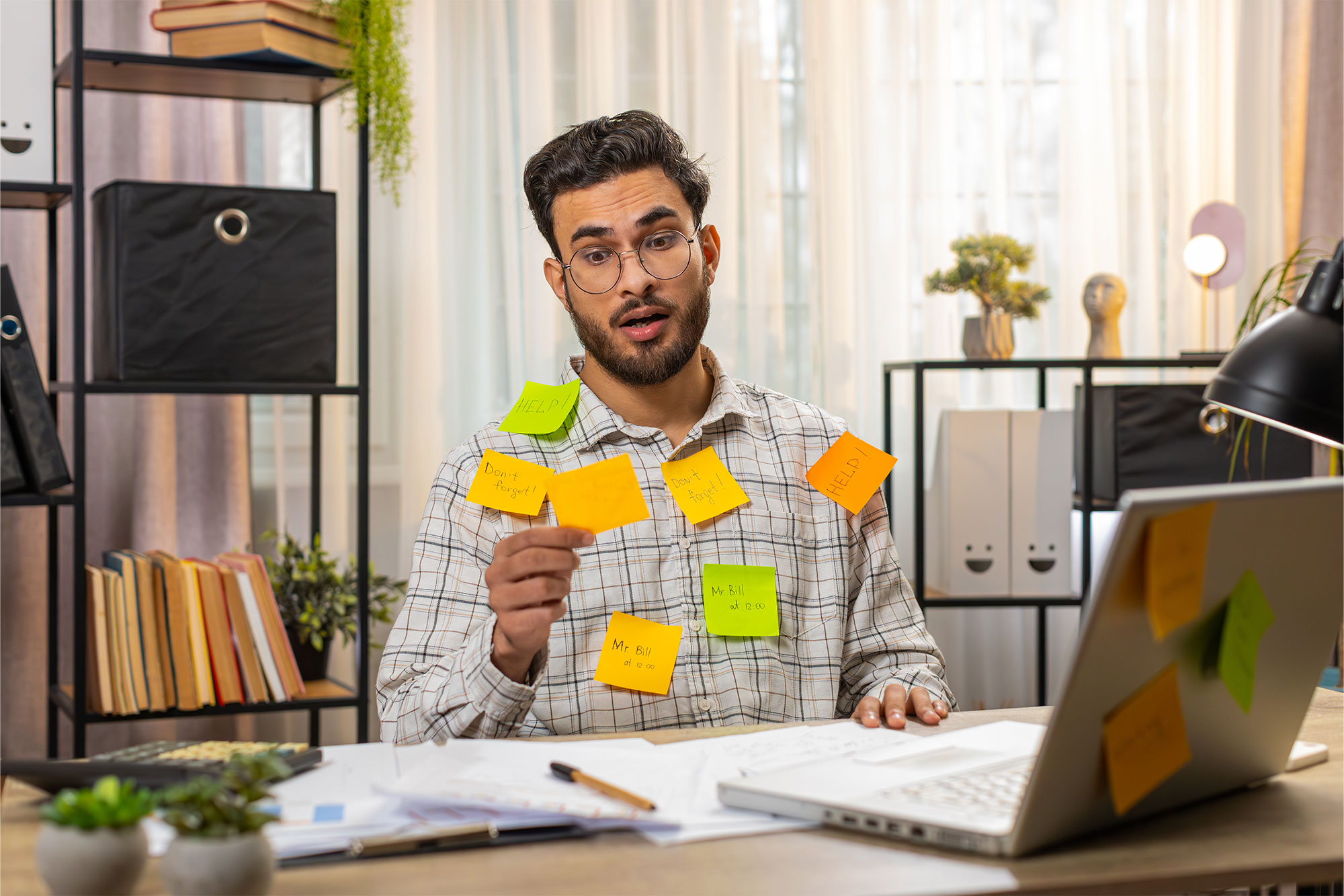 hustle Overwhelmed man with sticknotes reminding him of bills all over his shirt, sitting at desk in office.