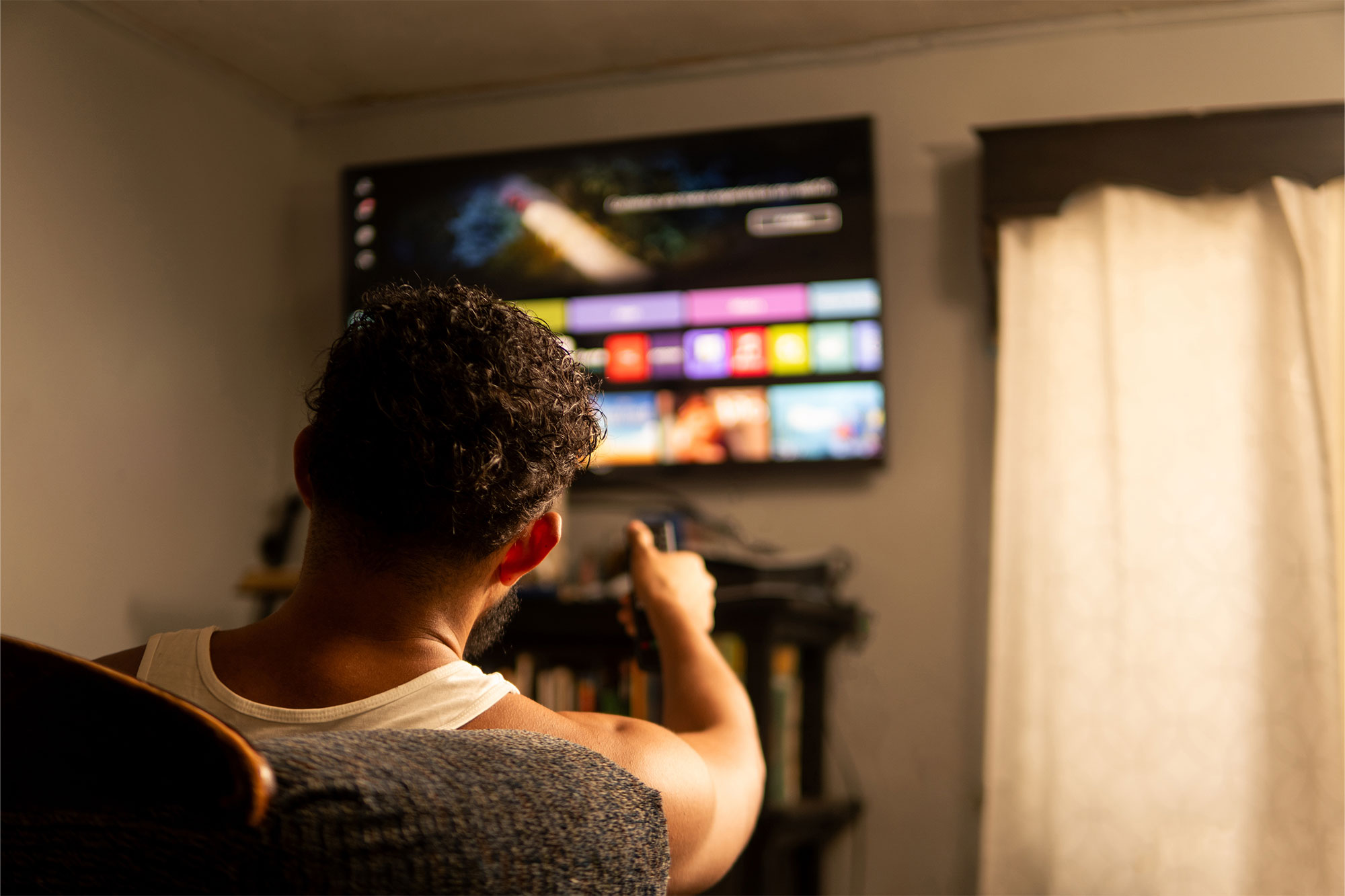 subscriptions Man sitting on couch pointing tv remote at smart tv.